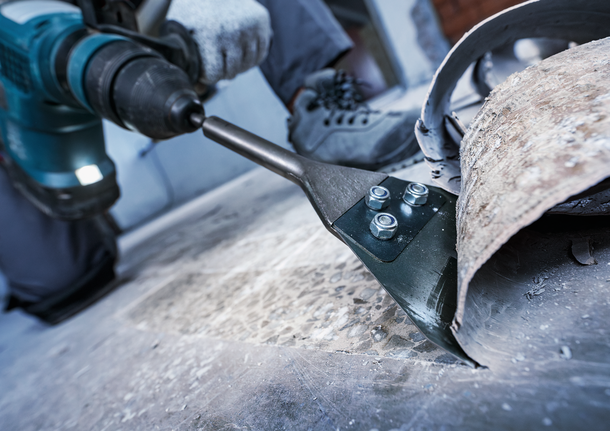 Person wearing safety equipment uses a power tool to remove flooring material.