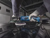 A person wearing safety equipment polishes a car hood with a blue polisher.