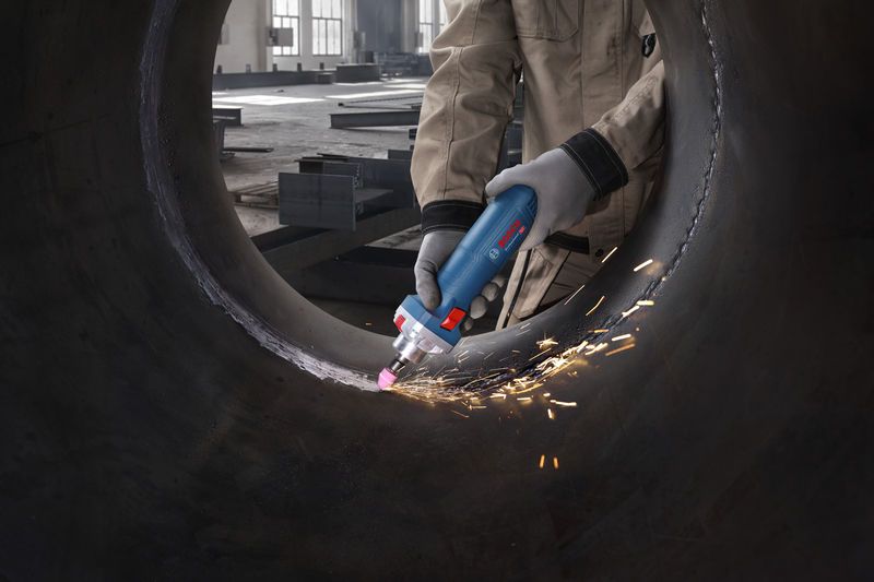 A person wearing safety equipment grinds the inside of a large metal pipe with a straight grinder.