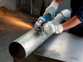 A person wearing safety equipment grinds a metal pipe with an angle grinder.