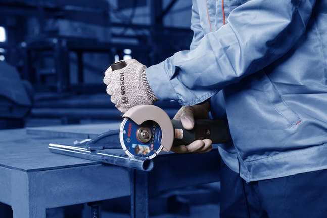 Person wearing safety equipment uses an angle grinder to cut a metal pipe.