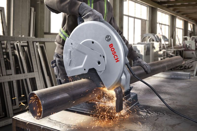 A person wearing safety equipment cuts a metal pipe with a chop saw.