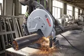 A person wearing safety equipment cuts a metal pipe with a chop saw.
