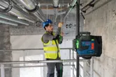 A person wearing safety equipment aligns pipes using a laser leveling tool.