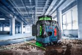Laser leveling tool projecting green lines on a dusty floor at a construction site.