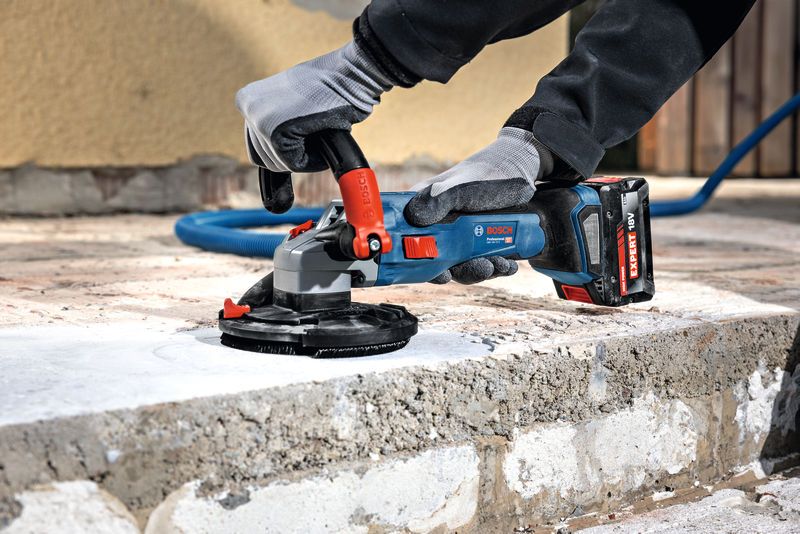 A person wearing safety equipment smooths concrete with a cordless grinder.