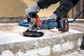 A person wearing safety equipment smooths concrete with a cordless grinder.
