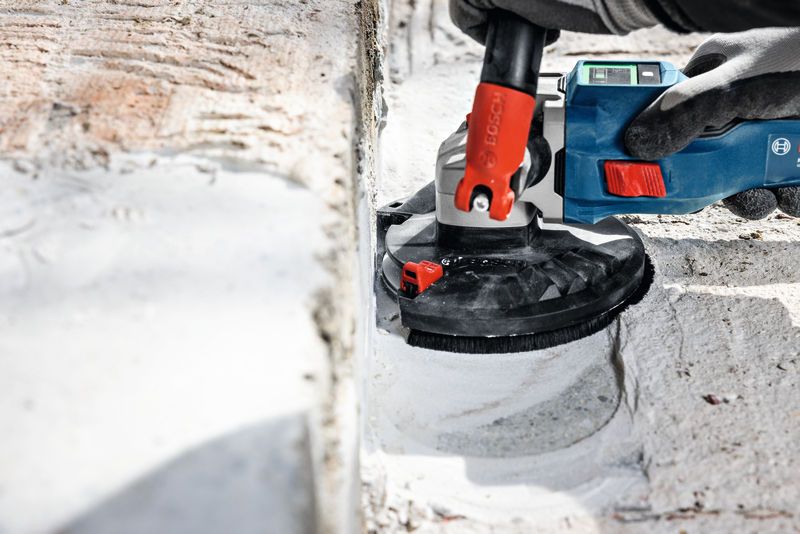 A person wearing safety equipment grinds concrete with a blue power tool.