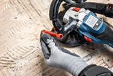 A person wearing safety equipment adjusts a concrete grinder on a textured floor.