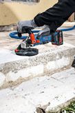 A person wearing safety equipment grinds concrete steps with a cordless concrete grinder.