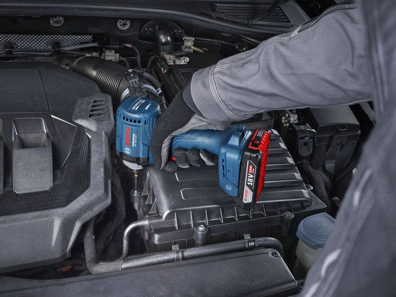 A person wearing safety equipment uses a cordless impact driver on a car engine.