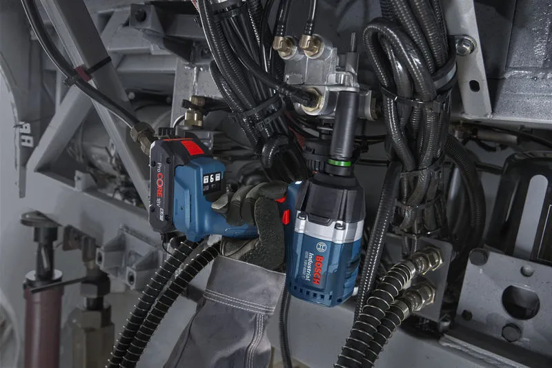 A person wearing safety equipment uses an impact wrench to tighten bolts on machinery.