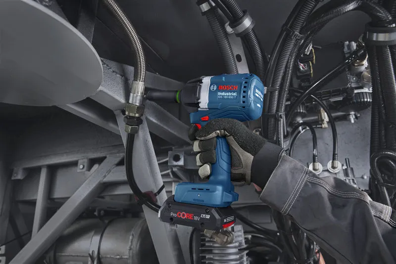 A person wearing safety equipment uses a cordless impact wrench on industrial machinery.