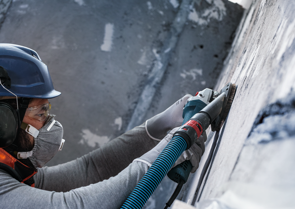 Person wearing safety equipment grinds a concrete wall with a power tool.