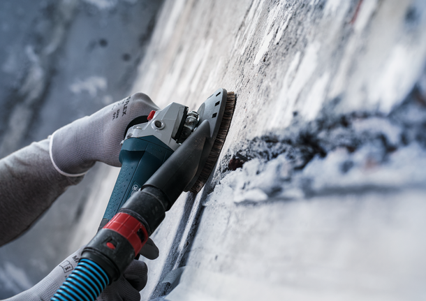Person wearing safety equipment polishes a concrete wall with a power tool.