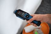 A person uses a material moisture meter to check a white wall.