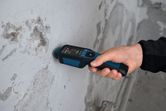 A person uses a material moisture meter to test a concrete wall.