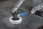 A person wearing safety equipment polishes a metal sheet using a power polisher.