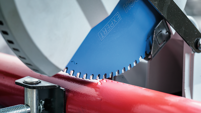 Circular saw blade cutting through a red metal pipe in a workshop setting.