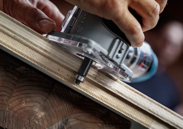Person trims the edge of a wooden board with a handheld router.