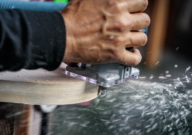 Person shaping wood with a handheld power router, creating dust and shavings.