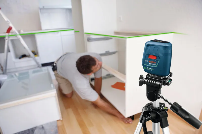 Laser leveling tool projects green lines while a person installs cabinetry.