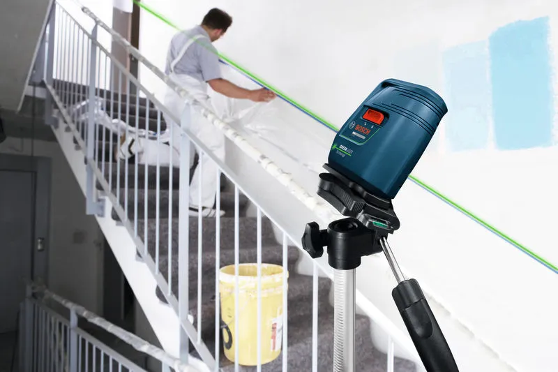 Laser leveling tool projects a green line while a person prepares a staircase for painting.