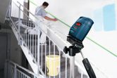 Laser leveling tool projects a green line while a person prepares a staircase for painting.