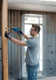 A person wearing safety equipment drills into a wooden beam during construction.