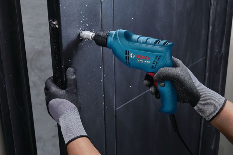 A person wearing safety equipment drills a hole into a metal surface.