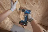 A person wearing safety equipment drills a screw into a wooden panel.