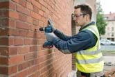 A person wearing safety equipment drills into a brick wall.