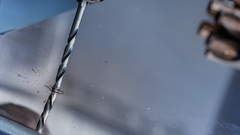 Person drills into a metal sheet.