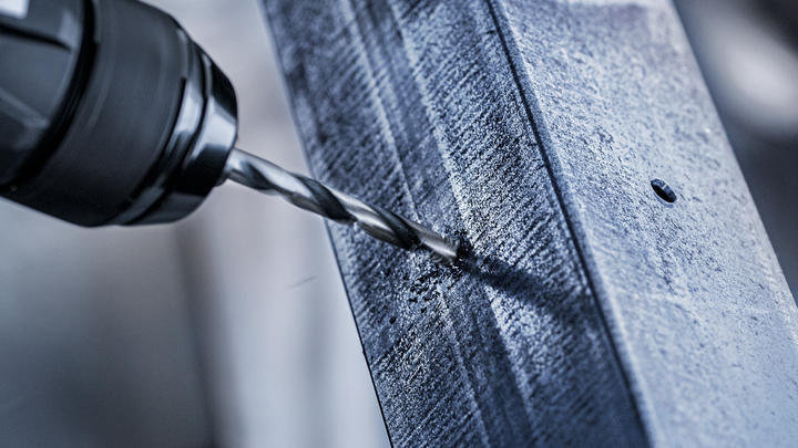 A power drill creates a hole in a metal beam.