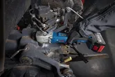 A person wearing safety equipment uses a cordless impact wrench on machinery.
