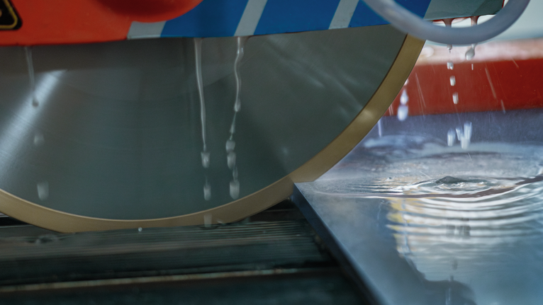Large circular saw blade with water cutting through a smooth tile surface.