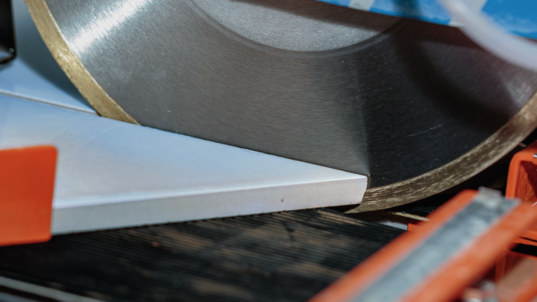Tile cutter blade slicing a ceramic tile at an angle.