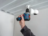 A person uses a cordless drill to install a security camera on a ceiling.