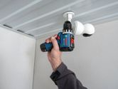 A person uses a cordless drill to install a security camera on a ceiling.