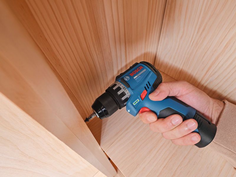 A person uses a cordless drill to drive a screw into a wooden surface.
