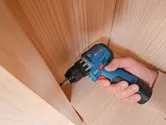 A person uses a cordless drill to drive a screw into a wooden surface.