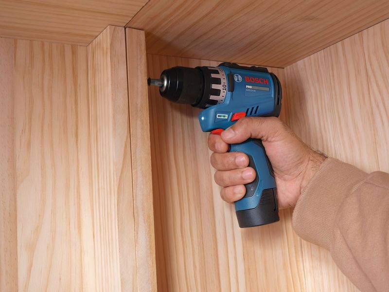 A person using a cordless drill driver to assemble a wooden cabinet.