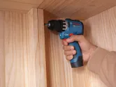 A person using a cordless drill driver to assemble a wooden cabinet.