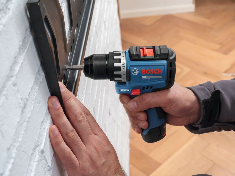 Person using a cordless drill to install a bracket on a white brick wall.