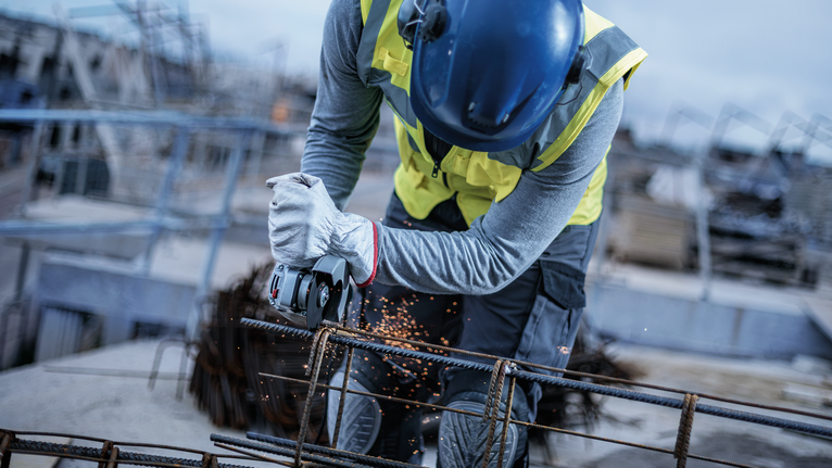 Person wearing safety equipment uses an angle grinder to cut through metal rebar.