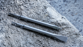 Two steel chisel bits rest on a rough concrete surface.
