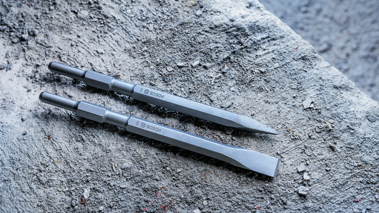 Two chisel drill bits lying on a rough concrete surface.