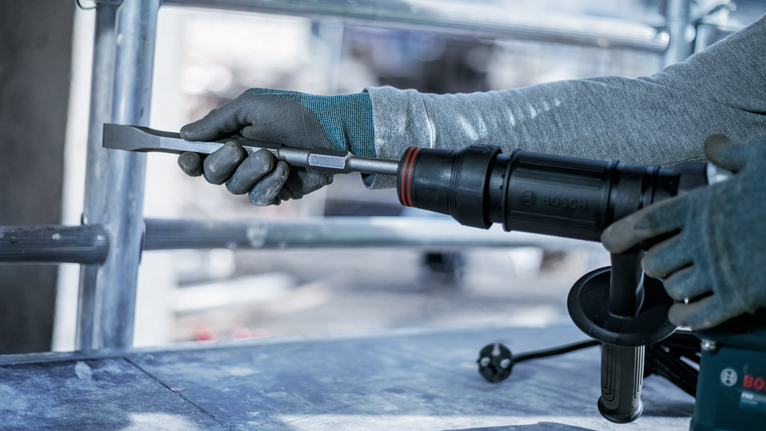 Person wearing safety equipment uses a rotary hammer with a chisel attachment.