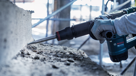 Person wearing safety equipment demolishes concrete with a rotary hammer.