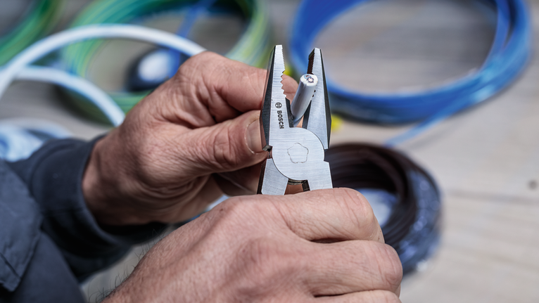 Person uses pliers to grip a wire with colored cables in the background.
